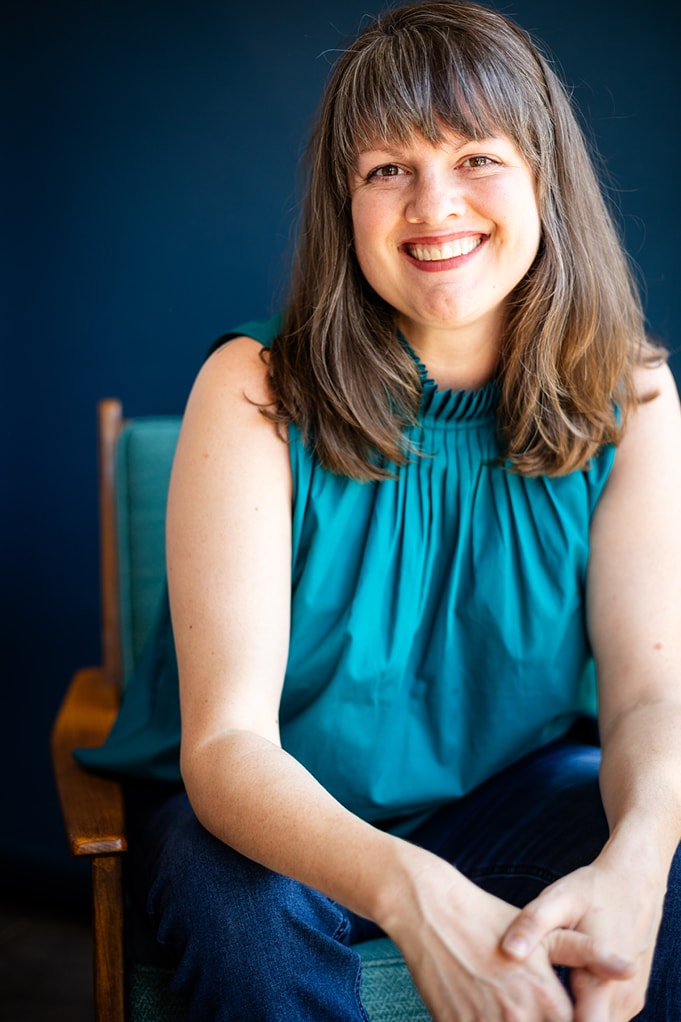 Amanda Edgar, facilitator of Page & Podium memoir writing courses, smiles and leans forward in a chair.